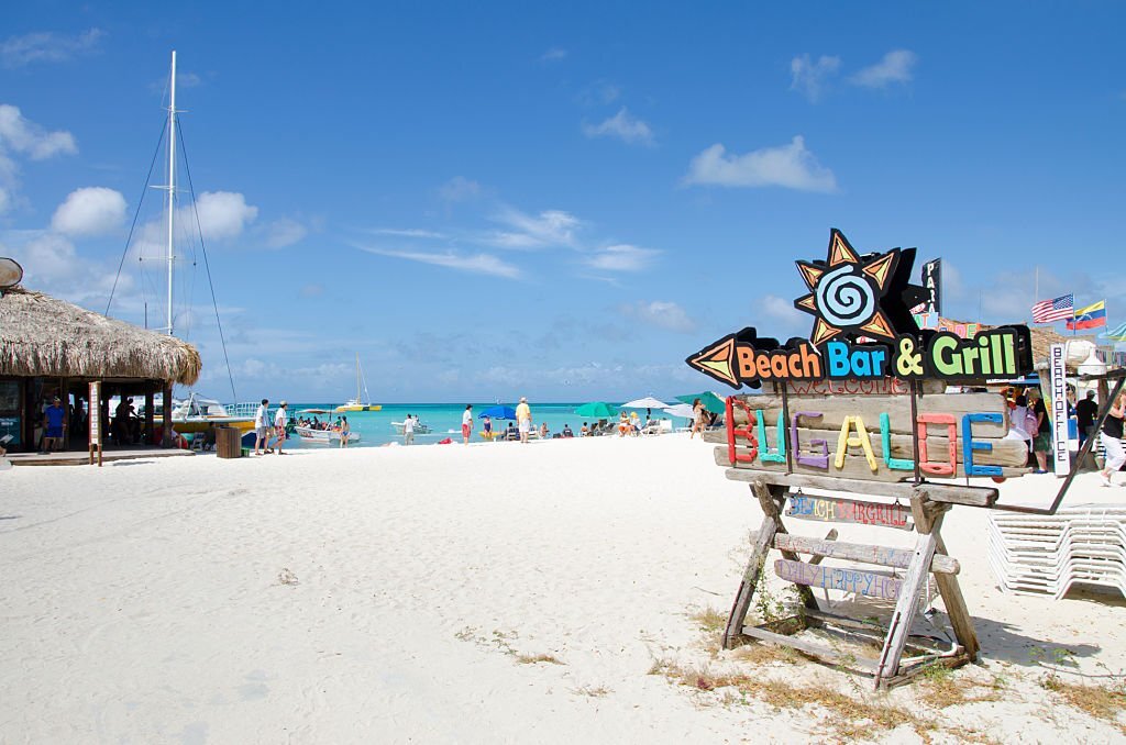 Sign of a bar at the beach where tourist relax and enjoys the turquoise colored water of the beach under a blue sky.