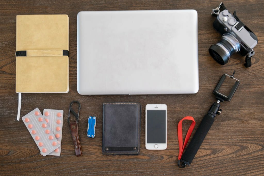 Travel Accessories Including, Laptop, Passport, Pills, Camera, Penknife, Phone, And Selfie Stick