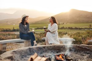 Shot of two women drinking wine while sitting by a fire pit