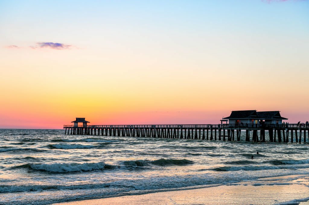 Naples, Florida sunset dusk in gulf of Mexico with pier wooden jetty on horizon and silhouette ocean waves view