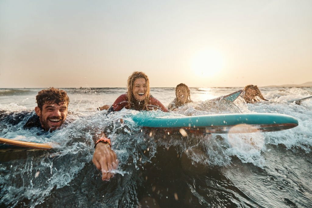 Cheerful surfers having fun during summer vacation in sea at sunset. Copy space.