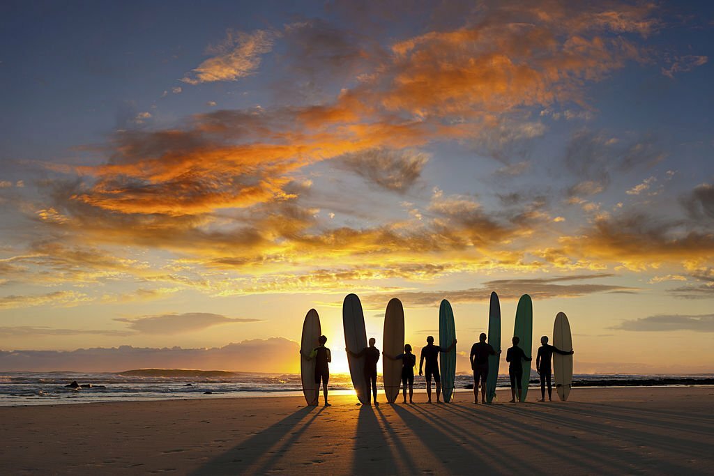 A group of young and old (longboard) surfers about to go surfing at sunrise.
