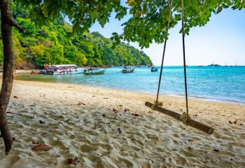 Surin Islands Thailand with rainforest and beaches and a longtail boats moored on the beach and in the bay.