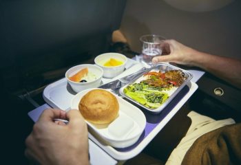 Traveling by airplane. Passenger enjoying dinner in economy class during long haul flight.